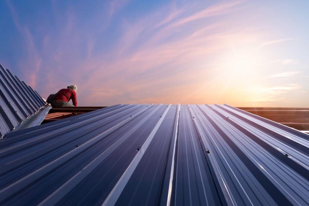 Construction worker standing on a roof covering it with metal.